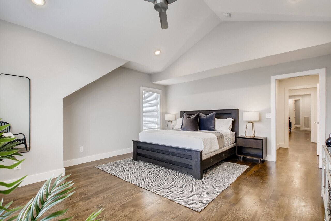 A bedroom with a bed, bedside tables, a ceiling fan, and a view of the hallway.