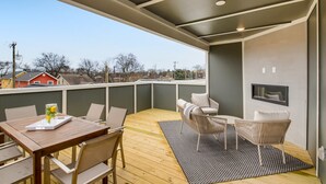 A modern outdoor deck with a wooden table and chairs, a small sofa, and a TV mounted on the wall.