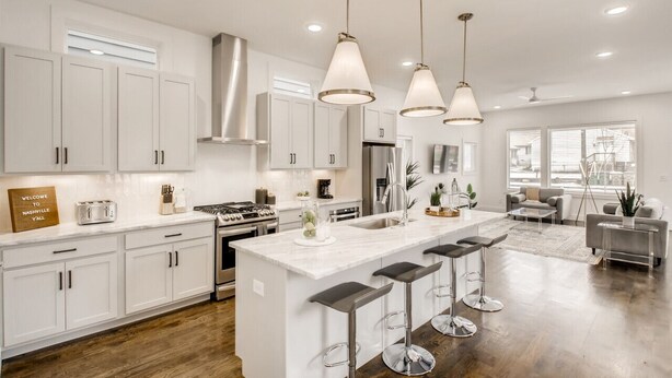 A modern kitchen with white cabinetry, a central island with bar stools, stainless steel appliances, and pendant lighting.