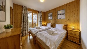 Een kamer met houten lambrisering, twee bedden, een nachtkastje, een potplant en lijstjes met foto's aan de muur.