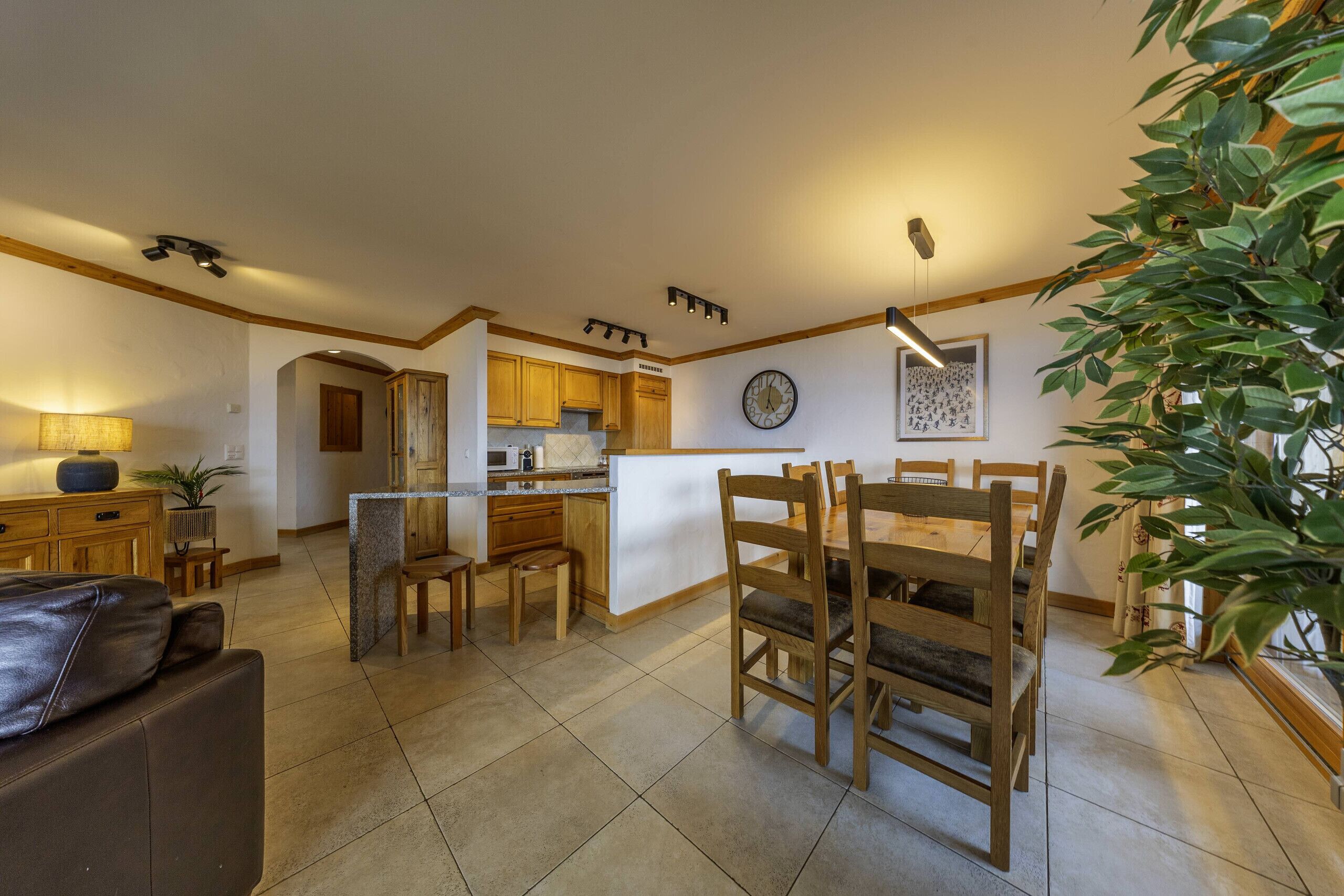 Un'ampia zona giorno con tavolo da pranzo, sedie in legno, divano e cucina sullo sfondo.