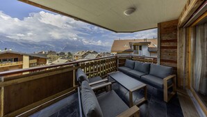 Een balkon met houten hekwerk, grijze zitting met kussens en een tafel.