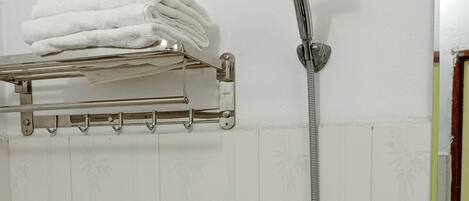 A shower with a handheld showerhead, a towel rack with folded towels, and a toilet with a red handle.