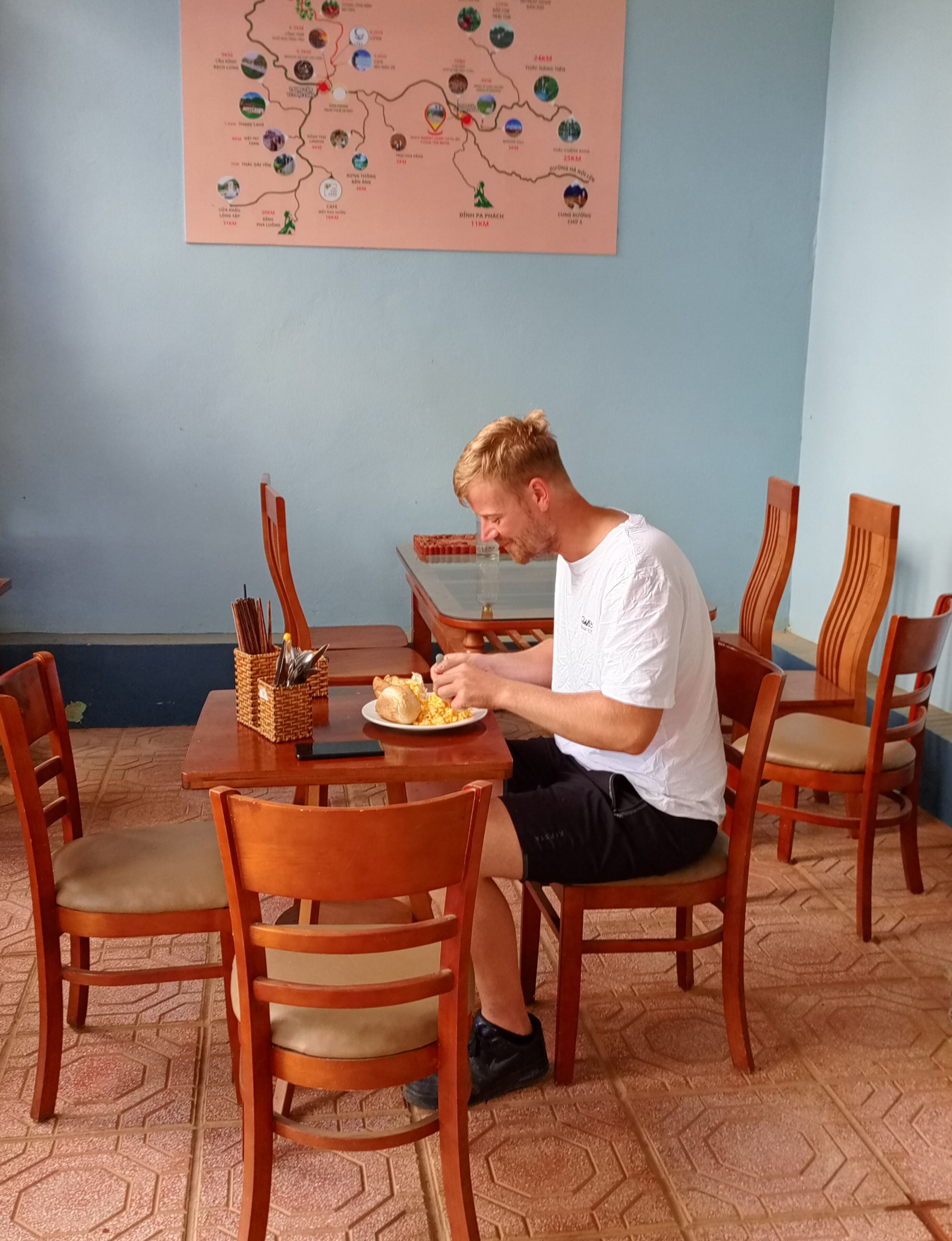 Eine Person sitzt an einem Holztisch mit einem Teller Essen, umgeben von Holzstühlen.