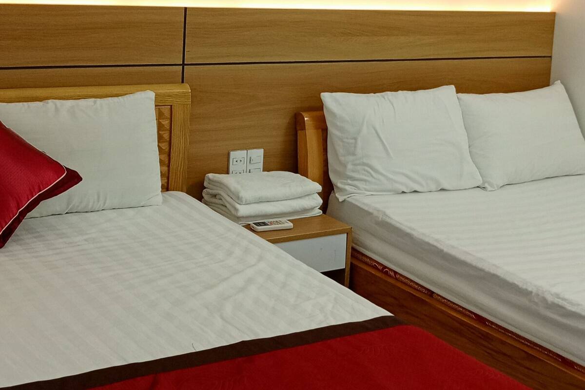 A hotel room with two beds, a nightstand, a wall-mounted lamp, and a wooden headboard.
