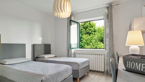 A modern hotel room with two beds, a large window with a view of greenery, a radiator, and a lamp on a bedside table. - NAT APARTMENTS Koper - Green All Around - Daisy and Tulip Apartments (Koper)