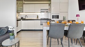 A modern kitchen with white cabinets, a dining table with chairs, and a small round table with a potted plant. - NAT APARTMENTS Koper - Green All Around - Daisy and Tulip Apartments (Koper)