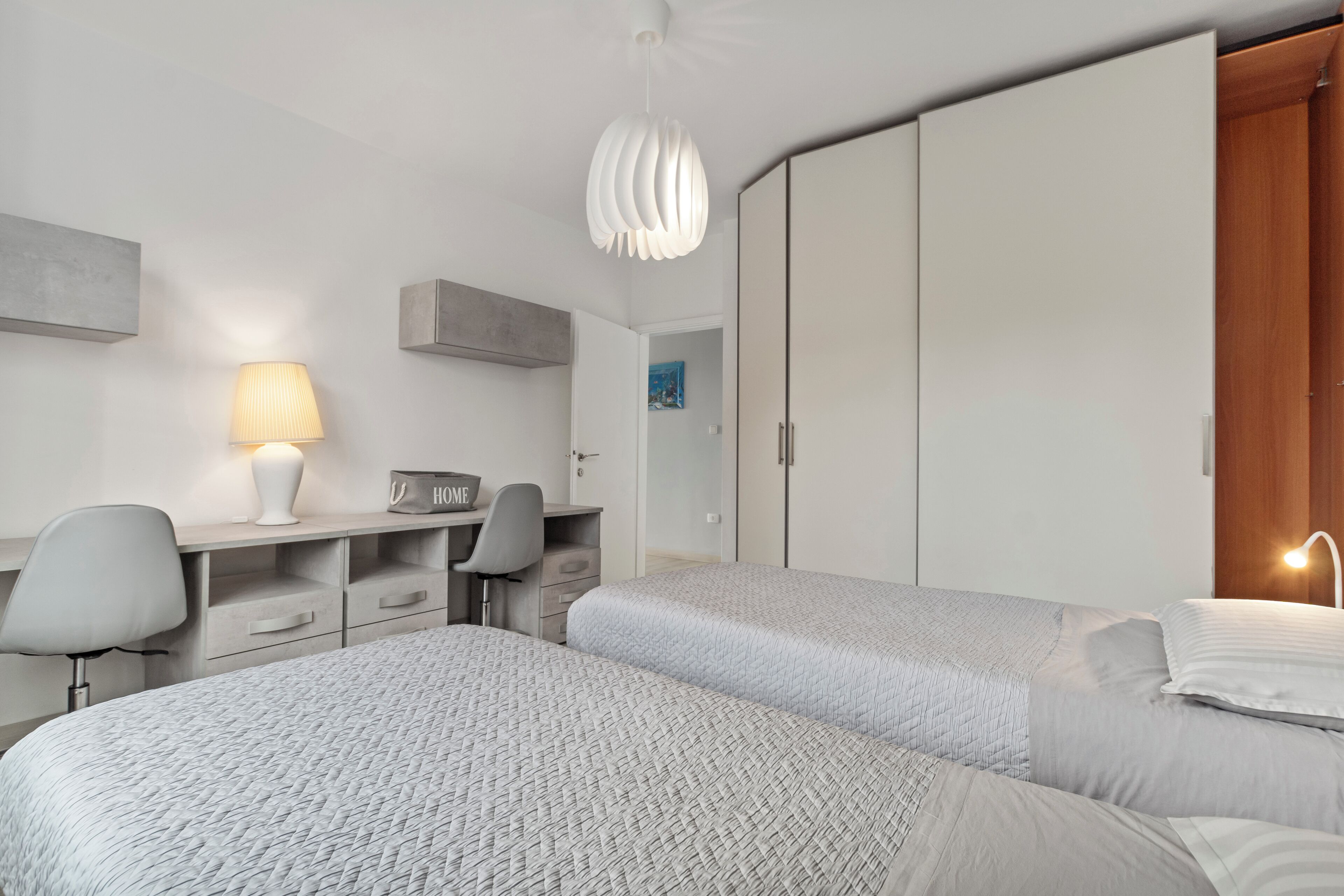 A modern bedroom with two beds, a desk, and a wardrobe.