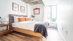 A modern bedroom with a wooden bed, white bedding, and a large window. - Rustique, NEW in Quebec city - 2 rooms + 2 bathroom (pool on roof during summer) (Québec)