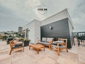 A rooftop terrace with modern furniture, including a sofa and chairs, and a view of the cityscape.
