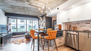 A modern kitchen with a dining area, featuring a large window, a chandelier, and a rustic ceiling. - Rustique, NEW in Quebec city - 2 rooms + 2 bathroom (pool on roof during summer) (Québec)