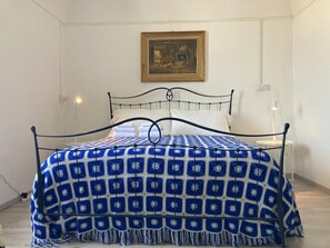 Un lit avec une couverture à motifs bleus et blancs, un oreiller blanc et un cadre en métal noir. Il y a un tableau accroché au mur au-dessus du lit.