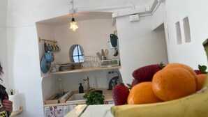Een keuken met witte wanden, een houten aanrechtblad en een hangende lamp. Er staan verschillende keukengerei en een schaal met fruit op het aanrecht.