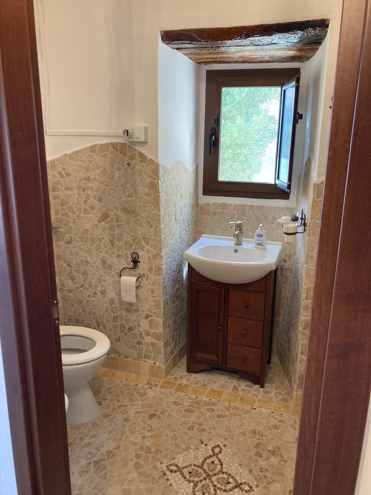 Un baño con pared de piedra, tocador de madera, lavamanos blanco y un inodoro.