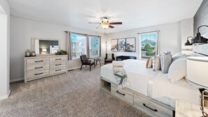 Une chambre à coucher comprenant un lit, une commode, une chaise, un bureau et un ventilateur de plafond.