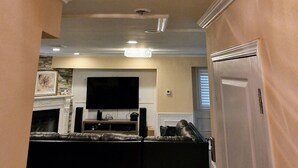 A spacious living area with a high ceiling, a chandelier, and a flat-screen TV mounted above a fireplace.