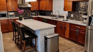 A modern kitchen with wooden cabinets, a marble island, and stainless steel appliances.