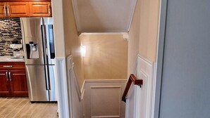 A narrow staircase leading to a landing with a kitchen area in the background.