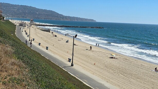 A coastal road with a beach on one side, a clear sky, and a distant hill.