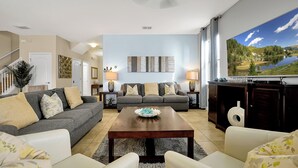 A living room with a grey sofa, a white sofa, a wooden coffee table, and a TV on the wall. - Unwind in Style: Spacious Villa with Game Room and Private Pool at ChampionsGate (Four Corners)