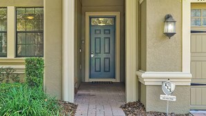 A beige building with a blue door, a mailbox, and a security sign. - Unwind in Style: Spacious Villa with Game Room and Private Pool at ChampionsGate (Four Corners)