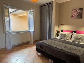 A bedroom with a bed, a window, a radiator, and a painting on the wall.