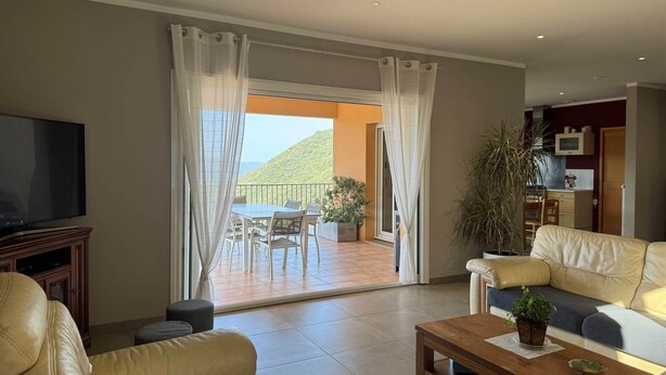 A living room with a television, leather sofas, a coffee table, and a balcony with a table and chairs.