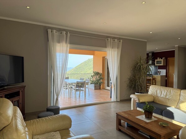 A living room with a television, leather sofas, a coffee table, and a balcony with a table and chairs.