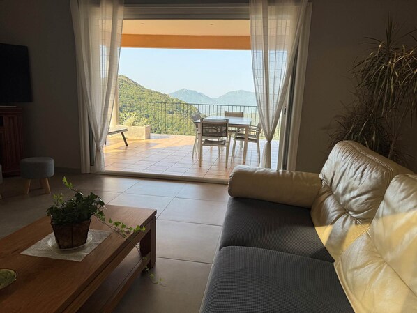 A living room with a sofa, a coffee table, and a view of a balcony with a table and chairs.