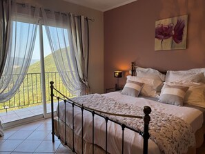 A bedroom with a bed, curtains, a nightstand, a lamp, and a painting.