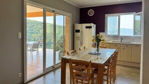 A modern kitchen with a dining area, a view of greenery through the sliding doors, and a clock on the wall.