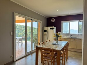 A modern kitchen with a dining area, a view of greenery through the sliding doors, and a clock on the wall.