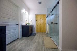 Ein Badezimmer mit Holztür, einer Glasdusche, einem Waschbecken mit Spiegel und einer Fußmatte.