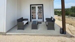 A covered patio with a white wall, a glass door, and outdoor furniture. - Family-Friendly Retreat in Canyon Lake (Canyon Lake)