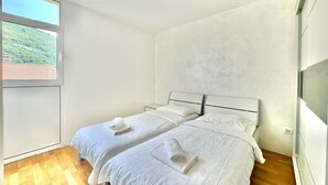 Un dormitorio con dos camas, un ventanal y vistas al exterior con vegetación.