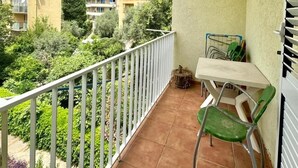 Un balcón con mesa y sillas, con vistas a un jardín y edificios.