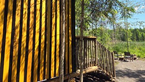 A wooden cabin with a yellow and black striped exterior, surrounded by trees and a gravel area with chairs. - Wood Duck Cabin, No Neighbours, Drive too, Pet Friendly (Golden Lake)