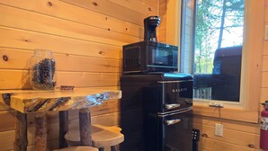 A compact kitchen with a black Galanz refrigerator, wooden tables, and a window with a view of trees. - Wood Duck Cabin, No Neighbours, Drive too, Pet Friendly (Golden Lake)