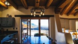 A dining area with a large wooden table, chairs, and a view of mountains through large windows.