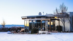 A modern house with a glass enclosure, surrounded by snow, with a view of mountains in the background.