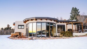 A modern house with a curved glass facade, outdoor seating, and a wooden deck.