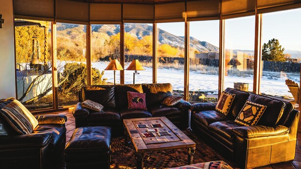 A cozy living room with leather sofas, a coffee table, and large windows offering a view of a snowy landscape and mountains.