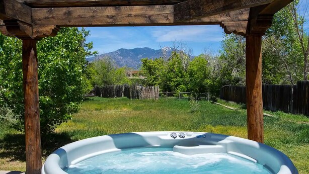 A hot tub under a wooden pergola with a mountain view in the background. - Casitas Encantadas - Charming home with Hot Tub in Taos (Taos)