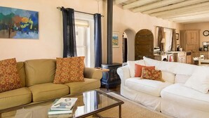 A living room with two sofas, a glass coffee table, a fireplace, and a kitchen in the background. - Casitas Encantadas - Charming home with Hot Tub in Taos (Taos)
