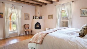 A bedroom with a large bed, wooden ceiling beams, a fireplace, and a bookshelf. - Casitas Encantadas - Charming home with Hot Tub in Taos (Taos)