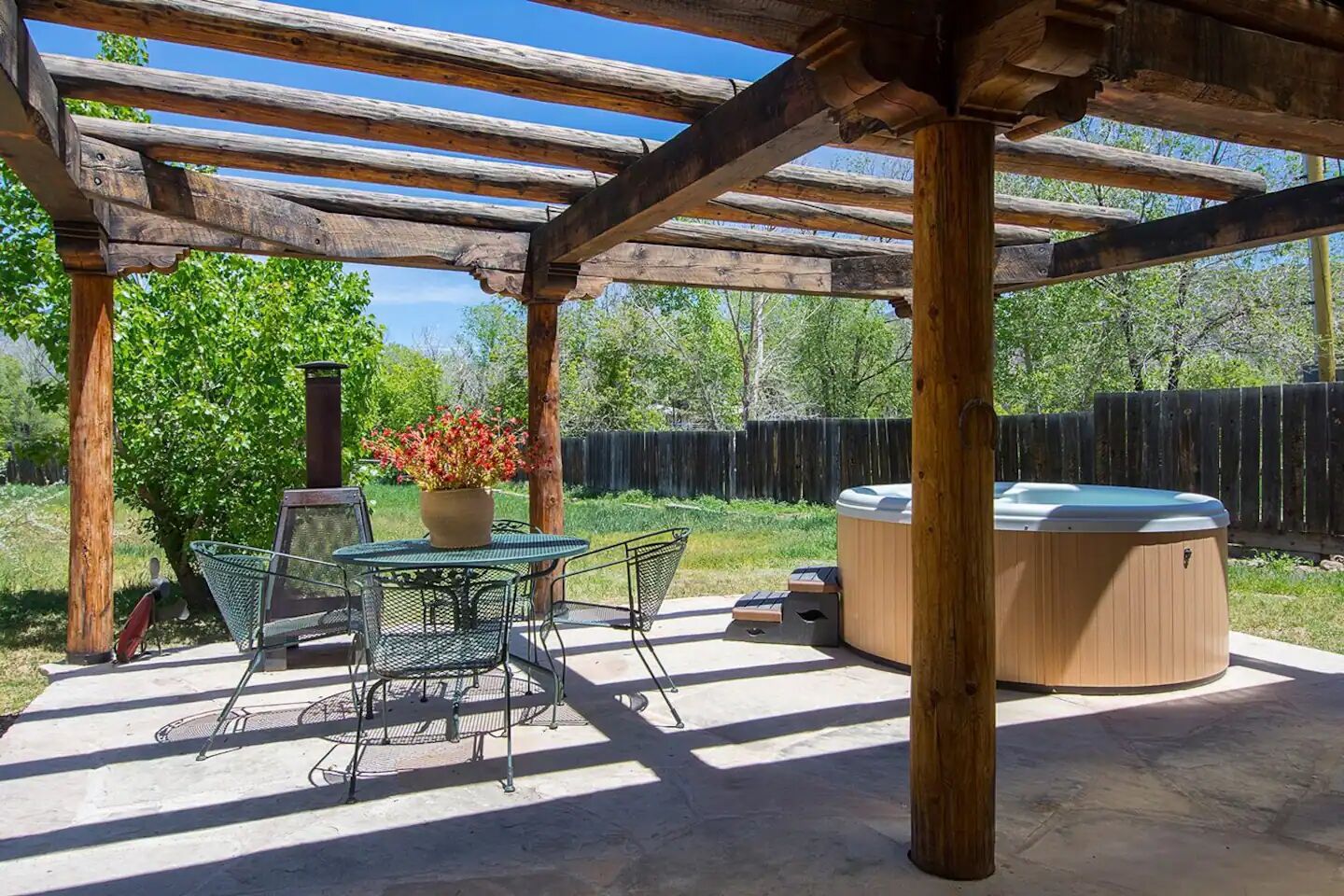 Eine überdachte Terrasse im Freien mit Tisch und Stühlen, einem Whirlpool und einer Holz-Pergola.