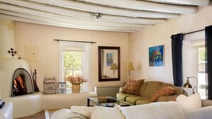 A cozy living room with a fireplace, a sofa, a coffee table, and a window with curtains. - Casitas Encantadas - Charming home with Hot Tub in Taos (Taos)