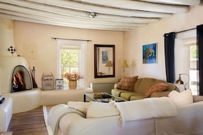 A cozy living room with a fireplace, a sofa, a coffee table, and a window with curtains. - Casitas Encantadas - Charming home with Hot Tub in Taos (Taos)