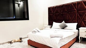 A neatly made bed with a red headboard, a bedside table, and a cat on the floor.