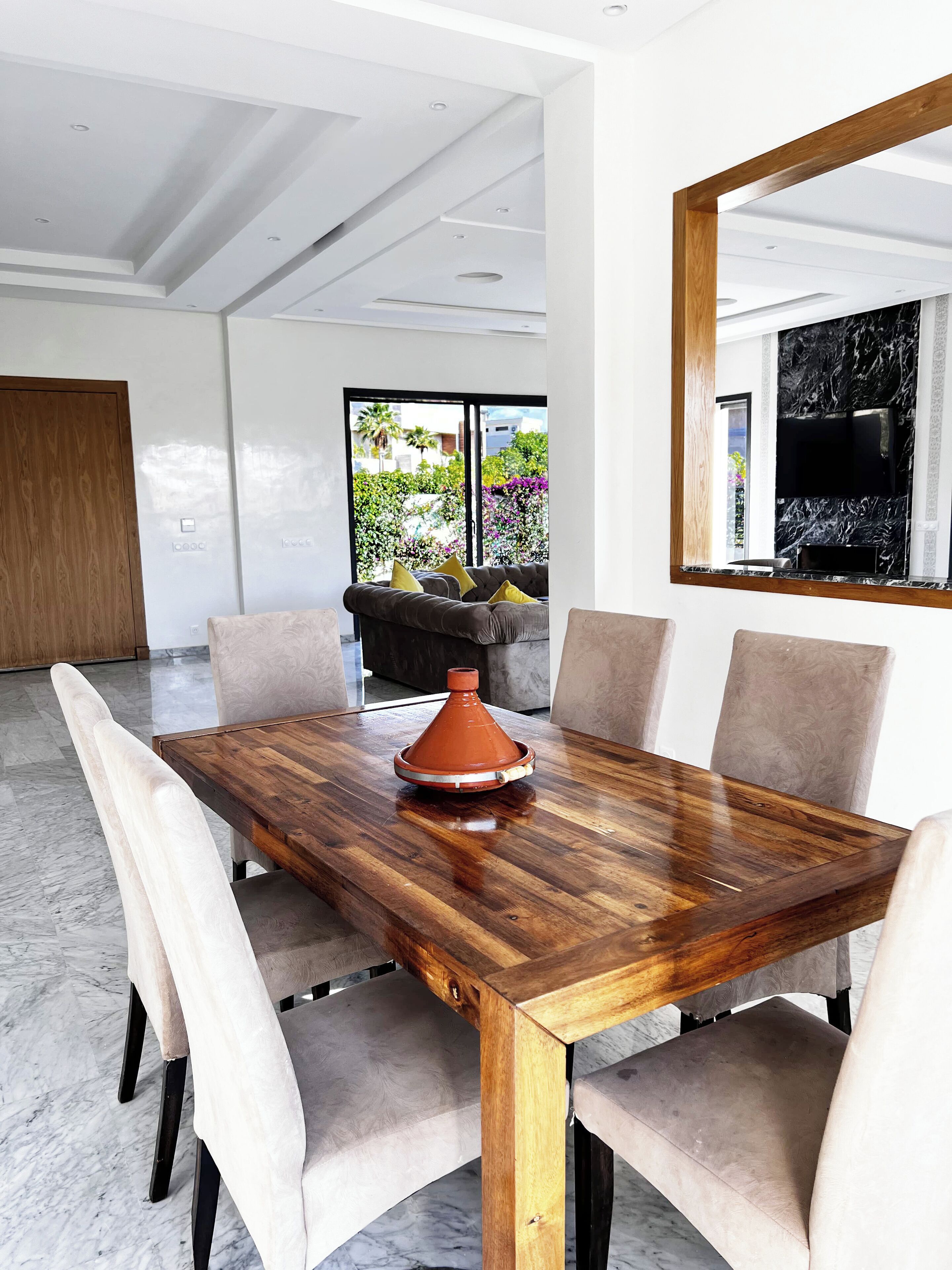 A modern dining area with a wooden table, beige upholstered chairs, and a large mirror.